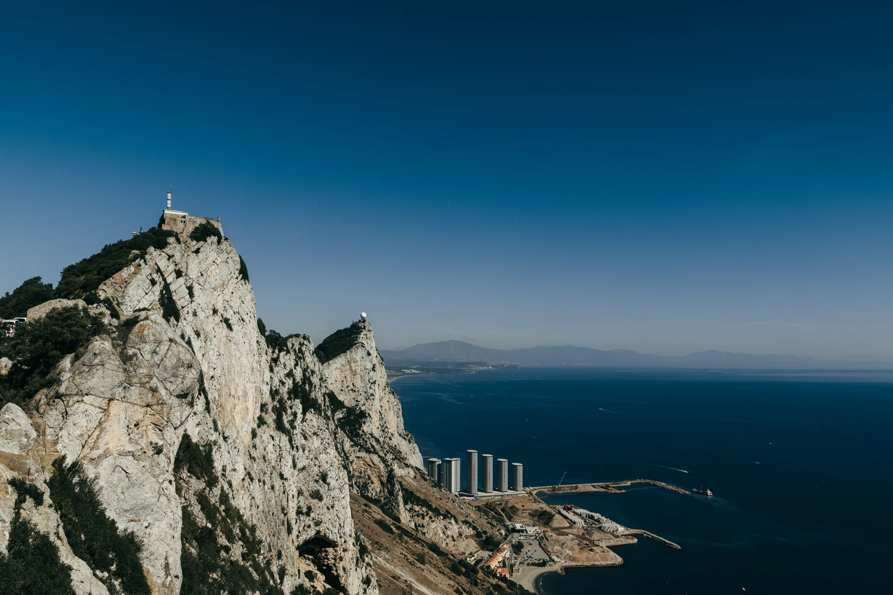 The jagged limestone ridge of the Rock of Gibraltar drops toward the sea under a deep blue sky.