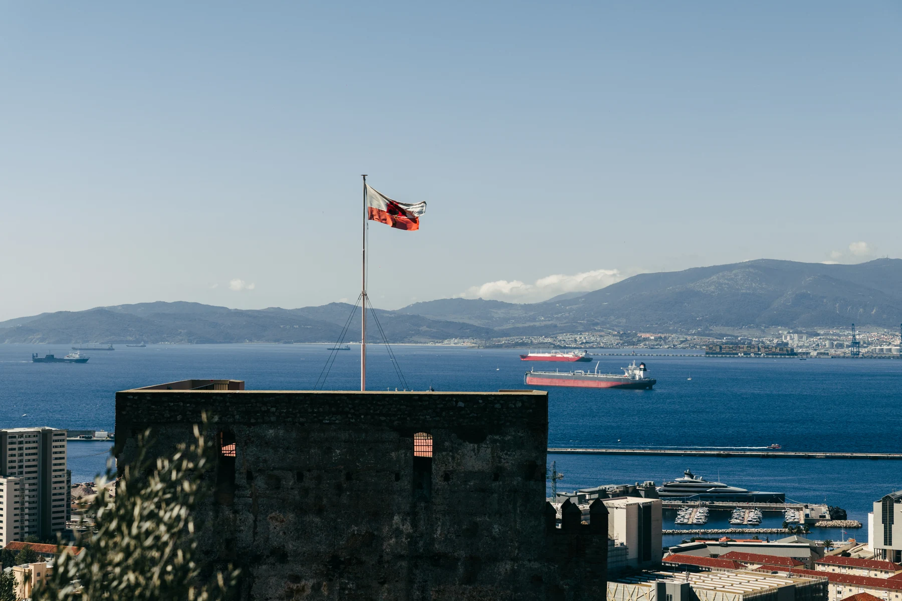 A tower of the Moorish Castle flies the flag of Gibraltar above the town, with the bay and the Spanish coast behind.