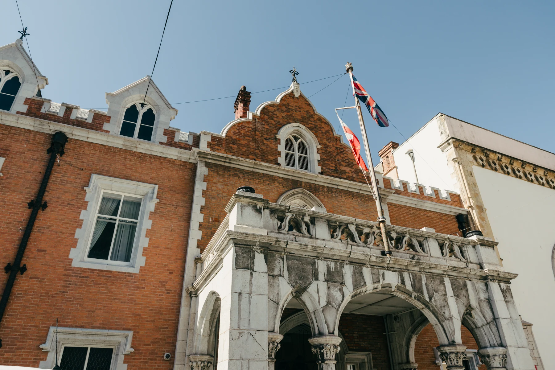 The red-brick facade and white stone porch of The Convent, the residence of the Governor of Gibraltar, with flags against a blue sky.