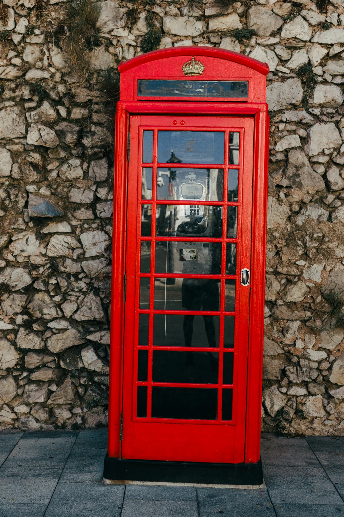 A classic red telephone box stands against a rough stone wall in Gibraltar.