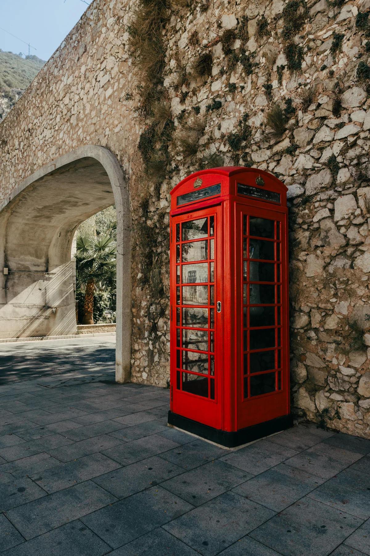 A red telephone box stands beside a stone archway in Gibraltar.